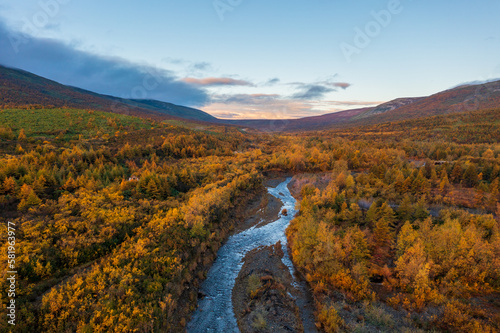Beautiful autumn landscape. Aerial view of a river in a mountain valley. Trees and bushes with yellow crowns. Traveling and hiking in northern nature. Magadan region, Siberia, Far East of Russia. © Andrei Stepanov