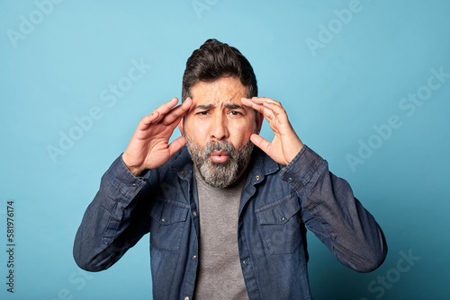 Vászonkép Mid-adult Latin man in a blue t-shirt, hands on his face, looking surprised and shocked by unexpected news or information