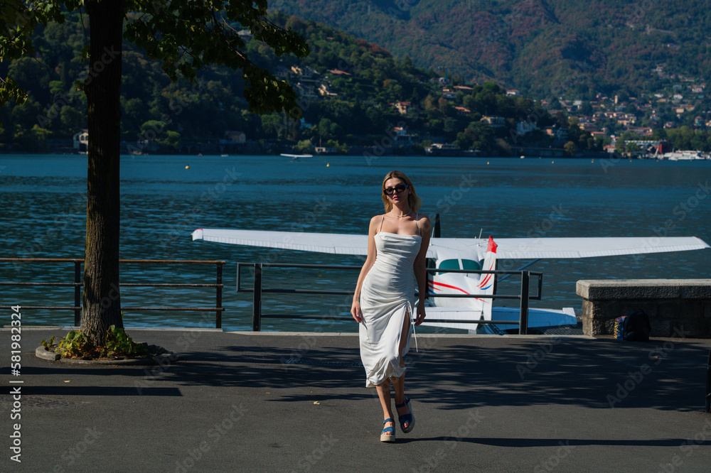 Fashion young woman in stylish dress walking near jet. Woman tourist getting out of jet airplane. Summer destination travel. Summer vacation on Como lake Italy. Travel and active lifestyle concept.