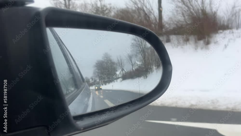 Side mirror of a car in winter in the snow in which a car is approaching on the road Side mirror of a car in winter in the snow in which a car is approaching on the road