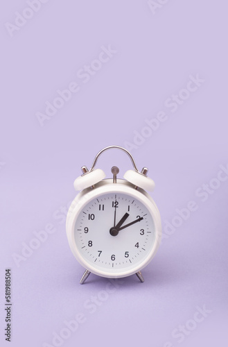 Reloj despertador color blanco ilustrando cambio de horario primavera, verano sobre fondo morado