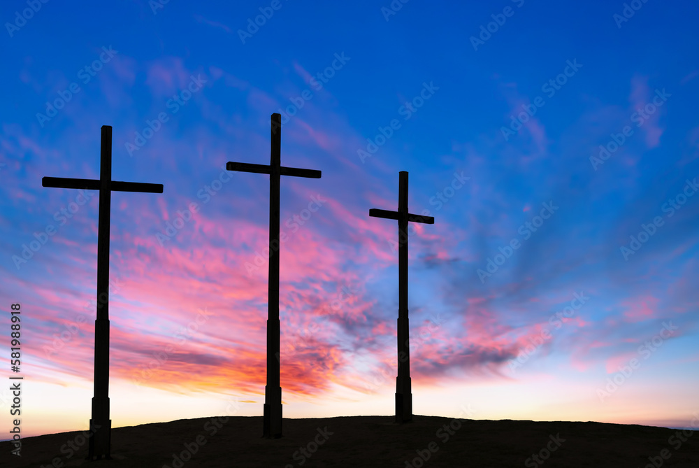Silhouettes of catholic crosses on top of hill against bright sunset sky Silhouettes of catholic crosses on top of hill against bright sunset sky