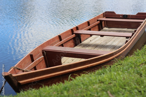 Um barco de madeira simples e bonito ancorado no lago próximo a margem com grama verde em um dia ensolarado photo