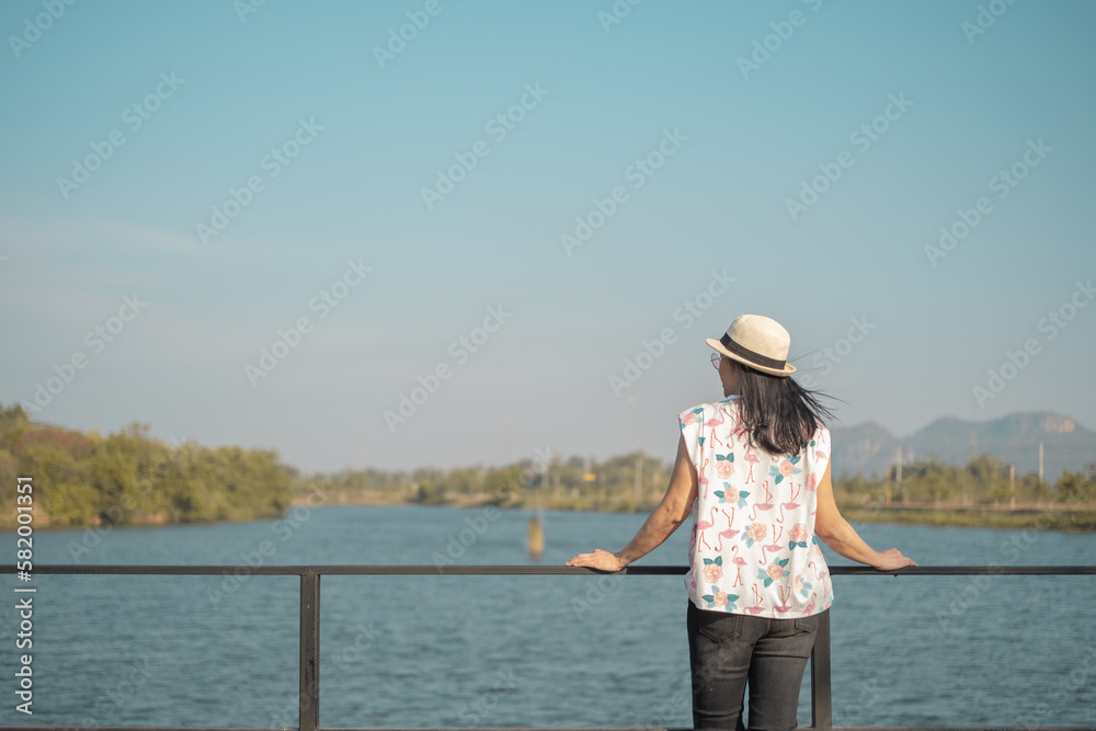 Asian woman with hat standing and enjoying the morning scenery by the lake with mountains