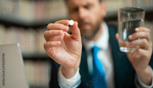 Close up portrait of man taking a medicine pill from headache migraine. Hand with medicine pill selective focus. Tired man suffering from headache after computer work.