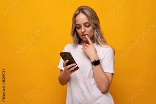 a woman in a white T-shirt with a smartphone in her hands uses an application on a yellow background