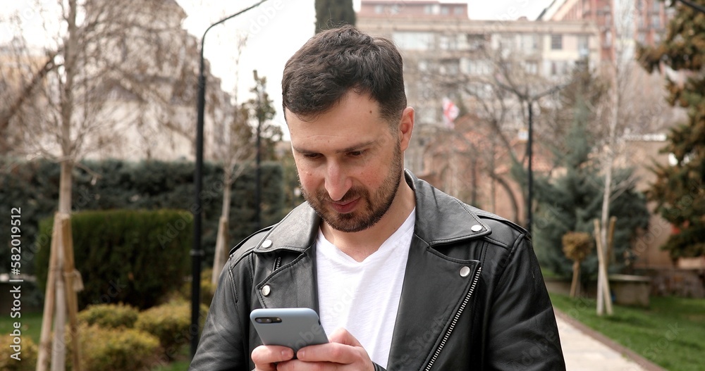 Handsome smiling young man dressed casually spending time outdoors at the city, using mobile phone while walking on street. Handsome smiling young man dressed casually spending time outdoors at the city, using mobile phone while walking on street.