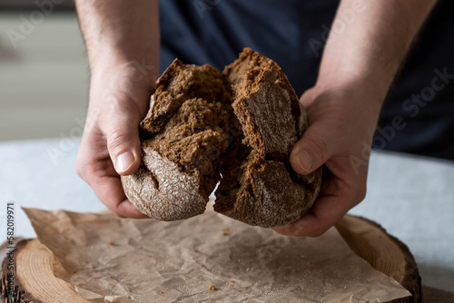 Fresh delicious bread in the hands of a male baker close-up. Freshly baked sourdough bread with a golden crust on a wooden board. The context of a bakery with delicious bread. Confectionery products.