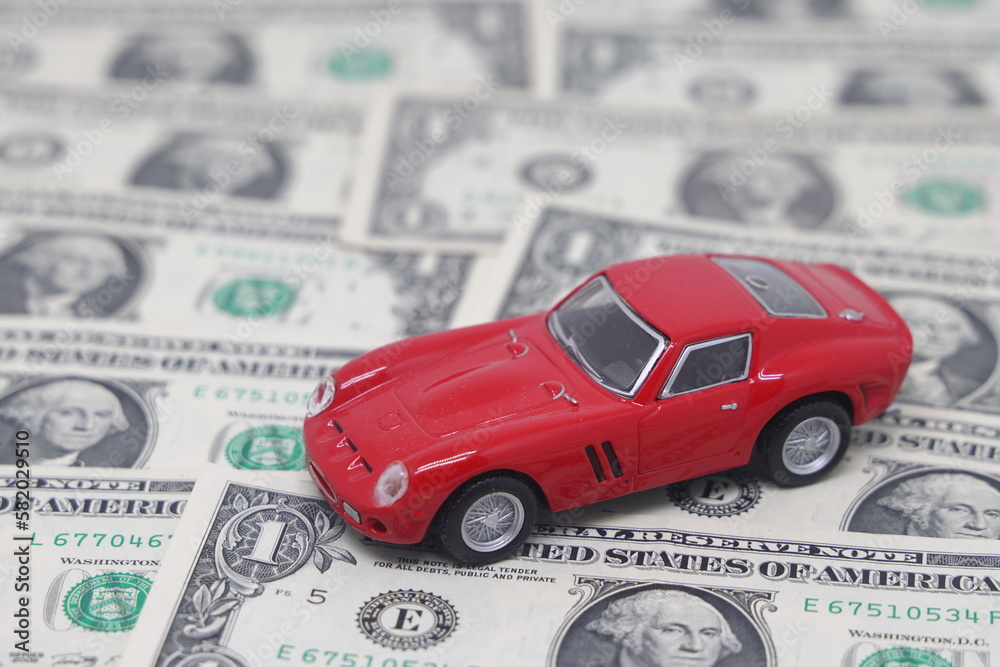 Small toy car on dollar banknotes in the form of a road, isolated on a white background, the cost of owning a car. Small toy car on dollar banknotes in the form of a road, isolated on a white background, the cost of owning a car.
