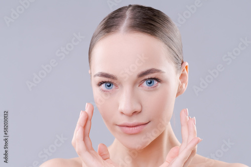 To camera isolated on background. Young woman close-up portrait. Healthy facial skin care beauty, age skin care cosmetic touches with hand, cosmetology concept