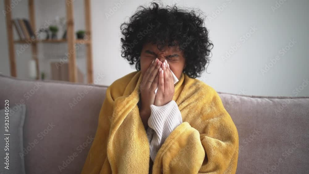 Sick, beautiful african american young woman sitting on sofa at home, have fever. In hand used tissues paper, blowing your nose, sneezing nose, runny. Health care, medicine. Virus, flu on cold season.
