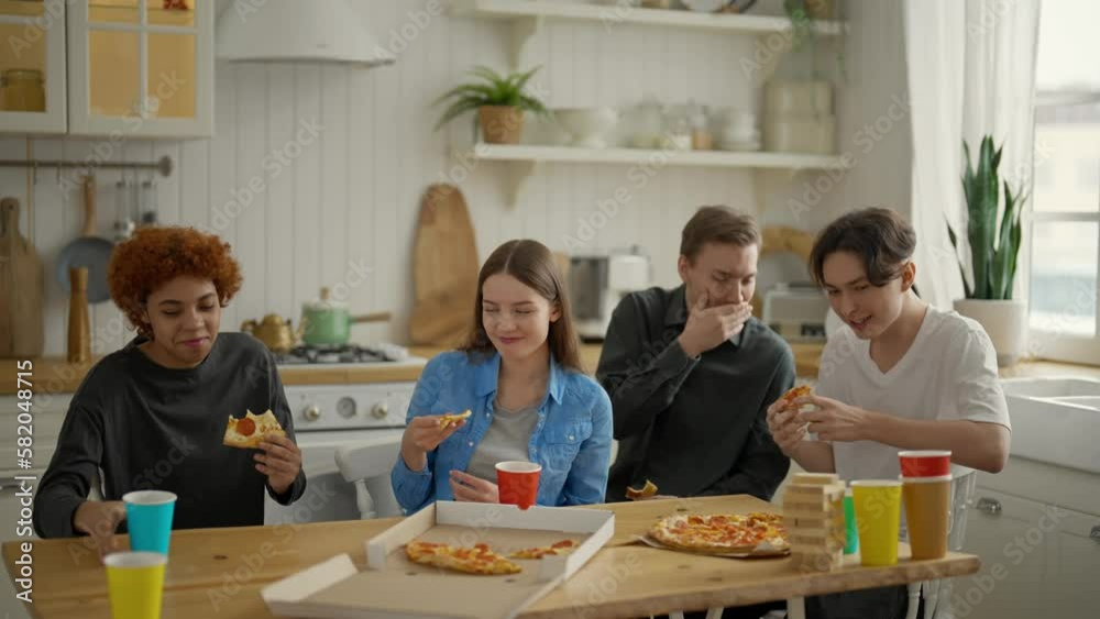 Hungry friends, students enjoying huge delicious pizza at kitchen home, open package and take piece. Food delivery service. Tasty fast food. Meeting, communication at weekend. Rest at company friends. Hungry friends, students enjoying huge delicious pizza at kitchen home, open package and take piece. Food delivery service. Tasty fast food. Meeting, communication at weekend. Rest at company friends.
