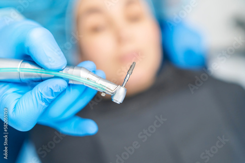 Fototapeta Naklejka Na Ścianę i Meble -  Closeup photo of dental implant in dentist hands with female patient in dental chair behind.