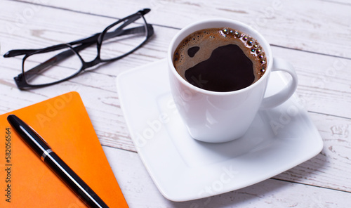 There is a notebook with a pen and a cup of coffee on the desktop.