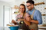 Young happy couple is enjoying and preparing healthy meal in their kitchen together