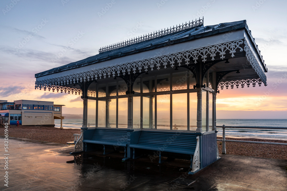 Victorian Shelter with the Pier Bandstand in the background at sunrise, Weymouth beach and seafront Promenade, Dorset.