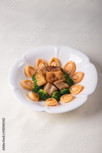 expensive premium braised head abalone with sea cucumber and flower mushroom broccoli in thick golden sauce on wood table asian chinese halal deluxe banquet seafood menu 