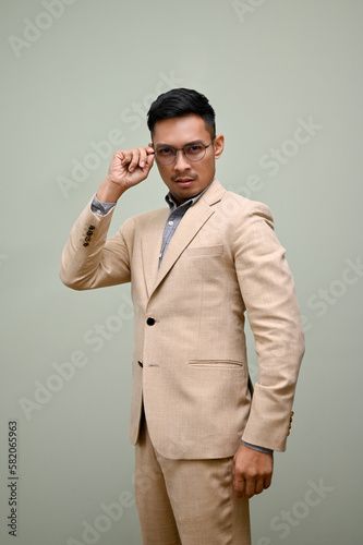 Determined Asian businessman touching his glasses while standing against an isolated background.