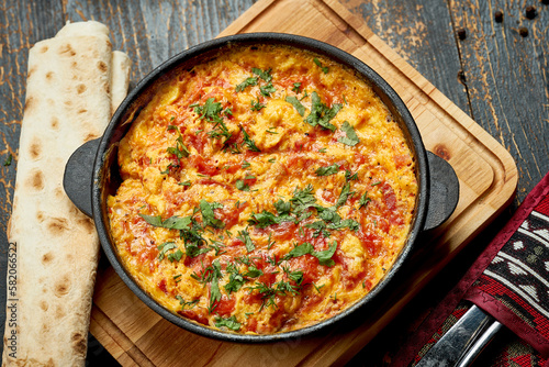 Menemen with eggs, tomato, green peppers, and spices served with bread in pan. Turkish breakfast