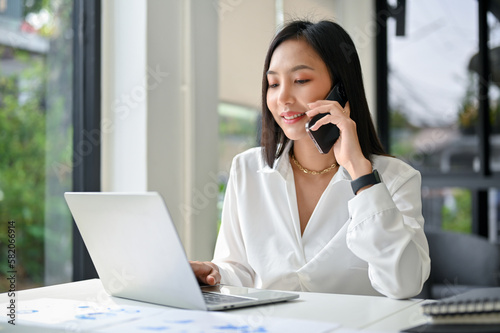 Attractive Asian businesswoman talking on the phone with her business partner