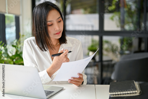 Foto Focused Asian businesswoman reviewing business document or analyzing financial d