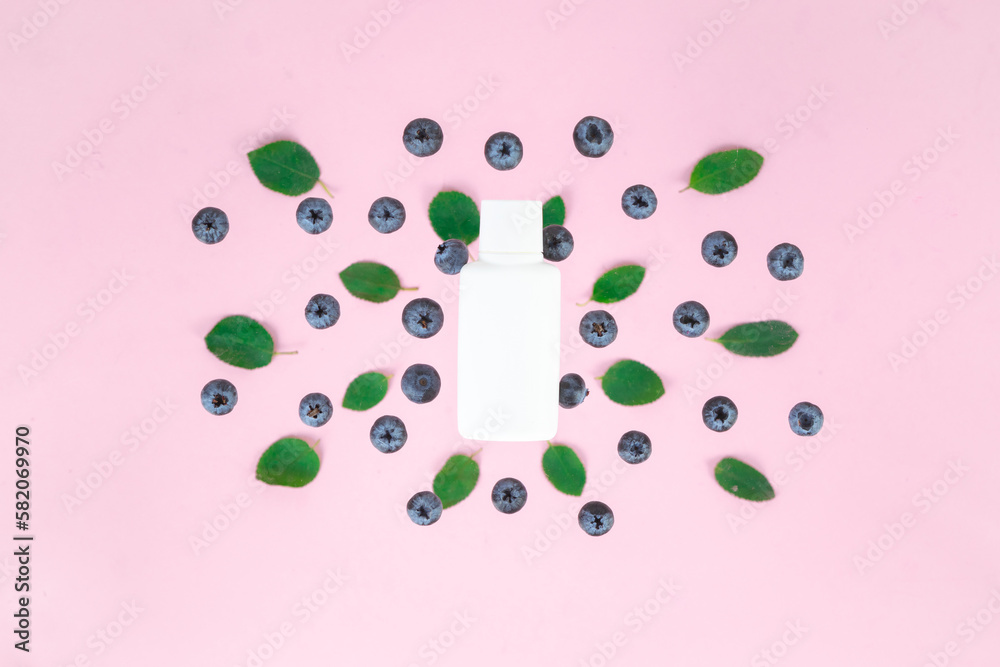 Ripe blueberries and green leaves near white tube. Pink background. Ripe blueberries and green leaves near white tube. Pink background.
