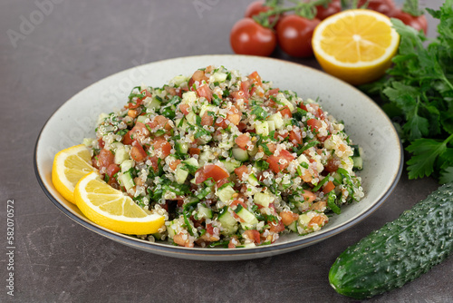 Vegan salad with quinoa, cucumbers, tomatoes, lemon, parsley on a brown background. Tabouleh salad. Middle Eastern cuisine