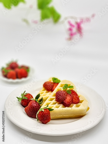 Selective focus of Waffles garnished with strawberries on a white plate with white background