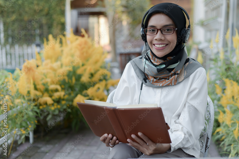 Portrait of happy asian muslim lady sitting using headset and read a book in coffee shop