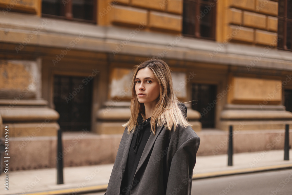 Photo of cute charming young woman wear grey jacket, calm walking outside city street. Girl look at camera. Photo of cute charming young woman wear grey jacket, calm walking outside city street. Girl look at camera.