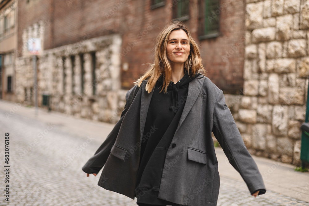 Young beautiful smiling hipster woman in trendy outfit. Sexy carefree woman posing on the street. Cheerful and happy girl wear grey suit and black hoodie turn around. Lifestyle, female beauty concept.