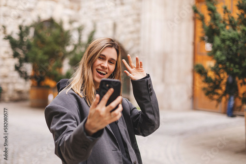 Woman waiving saying hello happy and smiling, friendly welcome gesture. Portrait of young beautiful attractive smiling cheerful girl taking selfie saying hello outside outdoors.