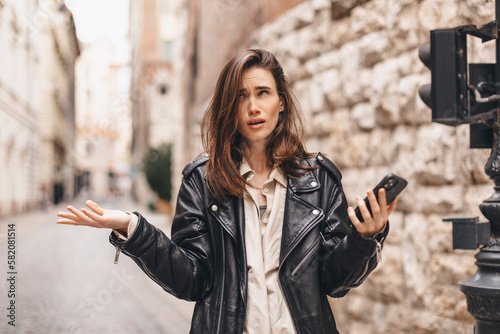 Explain wtf message mean. Portrait of frustrated questioned and annoyed young woman arguing over bad news shrugging spread hands in dismay sideways being displeased walking on the street in city.