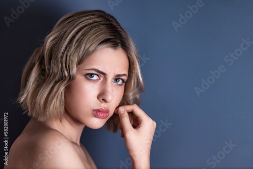 Close up portrait frowning woman, posing at dark gray background, looking at camera. Emotional face of lovely young blond lady isolated on blank studio wall. Human emotions concept. Copy ad text space