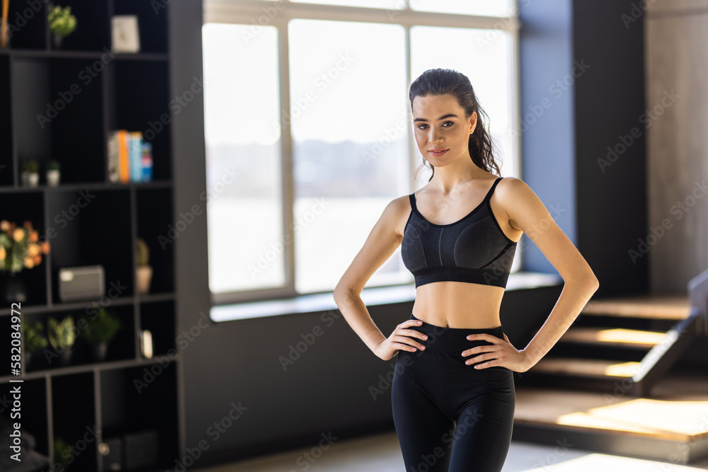 Smiling fitness woman athete in sport bra standing at home window