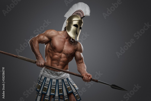 Shot of greek athlete with perfect body and spear dressed in plumed helmet.