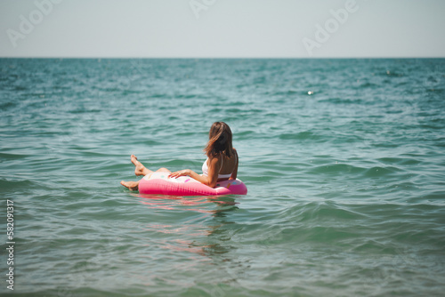 Young sexy woman in a slender body in a white swimsuit next to an inflatable mattress. Summer holidays. Rest on the sea. The concept of a healthy lifestyle. The girl is resting on the sea. 