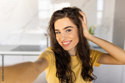 Young smiling beautiful positive ginger woman indoors at home take selfie by camera.