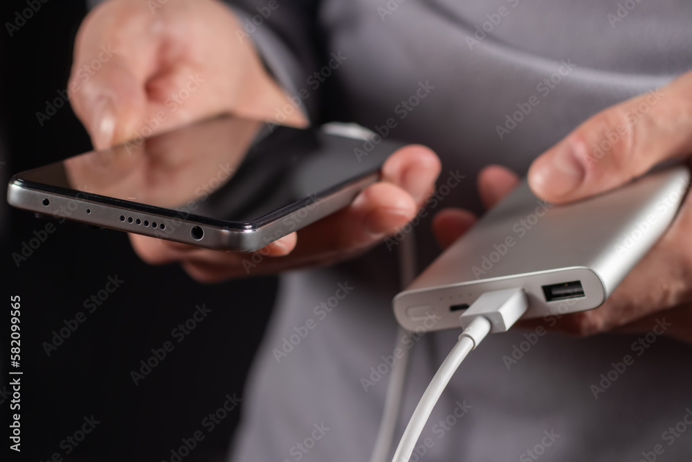 The men hand hold the phone and charger, powerbank and smart phone is connecting, energy The men hand hold the phone and charger, powerbank and smart phone is connecting, energy