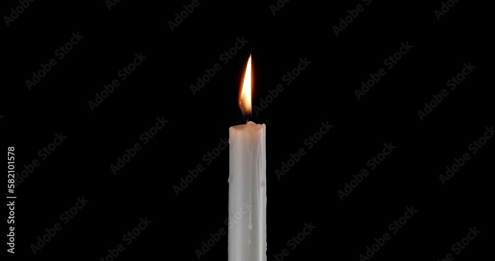 A single white candle burning. Isolated candle slow motion burning with dark background. White paraffin candle with yellow shades burns on a black background. Slow motion. A single white candle burning. Isolated candle slow motion burning with dark background. White paraffin candle with yellow shades burns on a black background. Slow motion.
