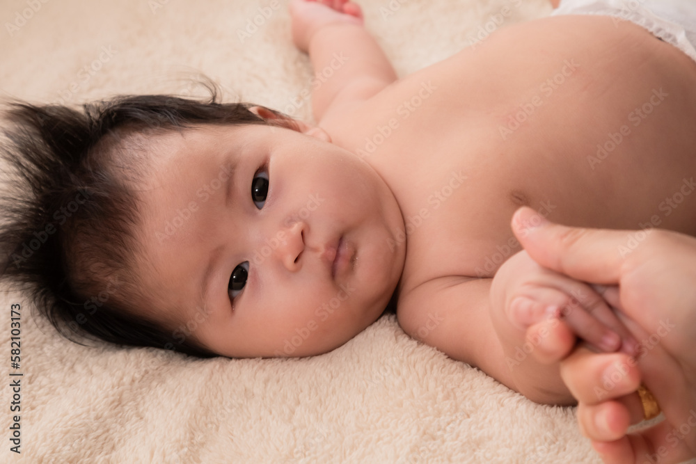 Selective focus of Asian newborn baby laying down on bed holding hand mother and looking mom with love and trust. Adorable infant sleeping on soft bed and parent touch baby with love. Selective focus of Asian newborn baby laying down on bed holding hand mother and looking mom with love and trust. Adorable infant sleeping on soft bed and parent touch baby with love.