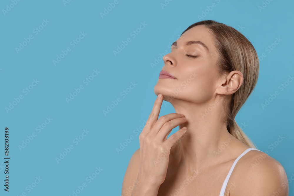 Woman massaging her face on turquoise background. Space for text