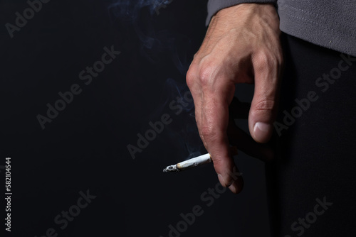 Hand with burning cigarette and smoke on black background
