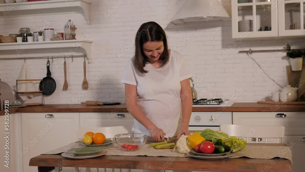 Close-up of a pregnant woman cutting fresh celery on a cutting board in the kitchen, she is preparing a fresh vegetable salad. Close-up of a pregnant woman cutting fresh celery on a cutting board in the kitchen, she is preparing a fresh vegetable salad.