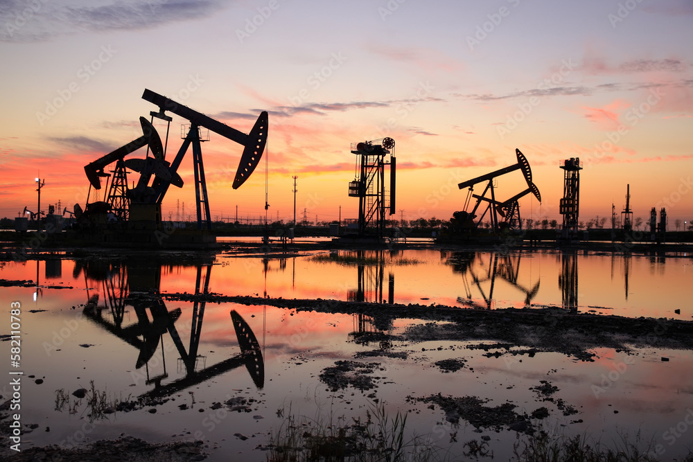 in the evening, oil pumps are running, The oil pump and the beautiful sunset reflected in the water, the silhouette of the beam pumping unit in the evening. in the evening, oil pumps are running, The oil pump and the beautiful sunset reflected in the water, the silhouette of the beam pumping unit in the evening.
