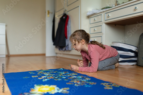 Little girl sitting on the floor and solving a picture puzzle photo