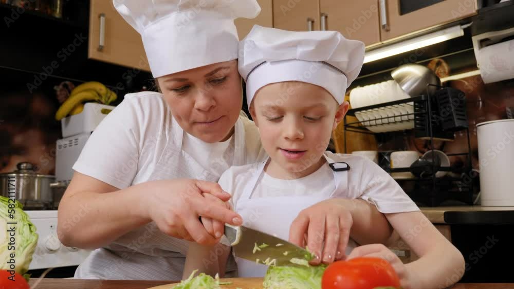 A happy mother teaches her little son how to cut cabbage, they hold a knife together and cut cabbage for a vegetable salad. A happy mother teaches her little son how to cut cabbage, they hold a knife together and cut cabbage for a vegetable salad.