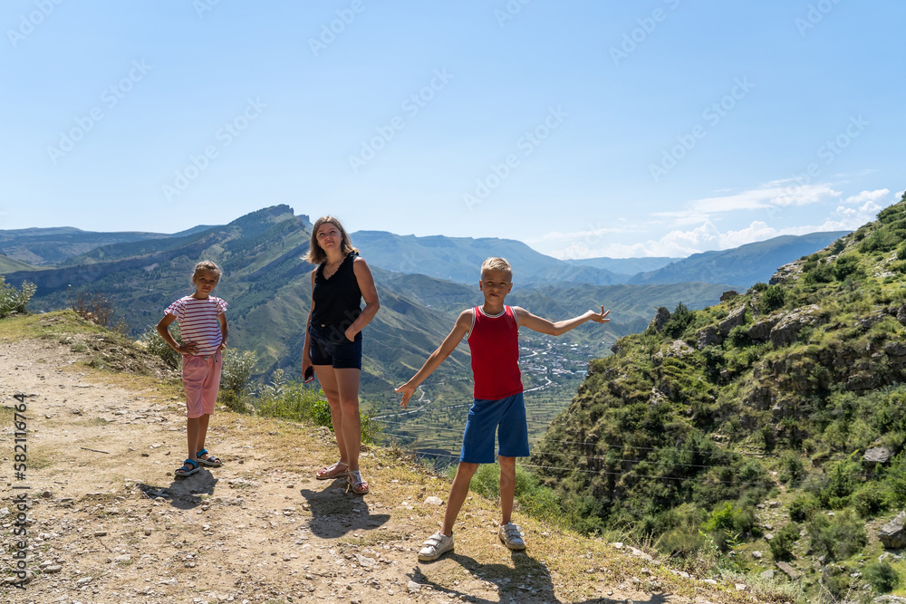 Cheerful mom, son and daughter are standing toghether at rock hiiltop in mountains. Fun happy lifestyle in summer