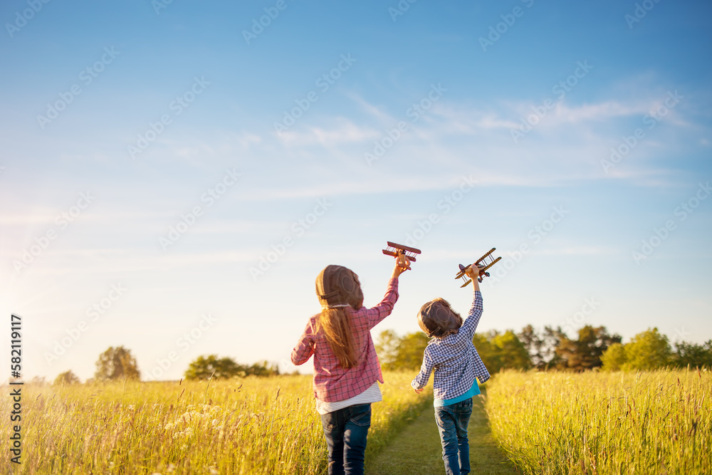 Boy and girl plaing with wooden planes on the field in sunset - obrazy, fototapety, plakaty 