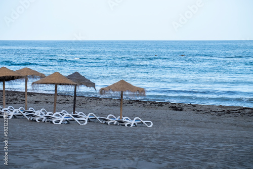 Straw beach umbrellas and comfortable sun loungers on Maditerranean's shore. photo